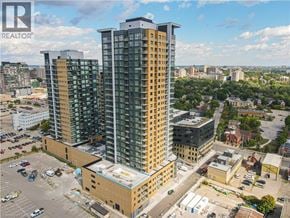 Kitchener condo for rent - A tall building with a glass facade stands in the foreground of a cityscape.