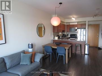 Toronto (Long Branch) condo for rent - A living room with a grey couch and a dining table with blue chairs.