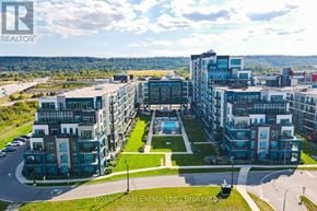 Grimsby (Grimsby Beach) condo for rent - A large, modern apartment complex with a pool in the center, surrounded by greenery and a clear sky.