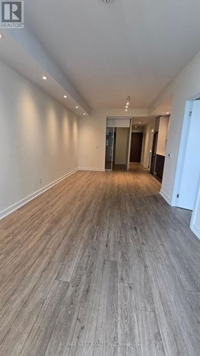 Toronto (South Parkdale) condo for rent - A spacious room with wooden flooring and white walls.