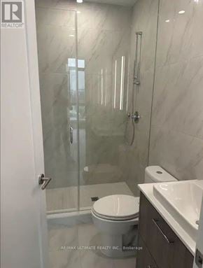 Toronto (Junction Area) condo for rent - A white toilet sits next to a sink in a marble bathroom.