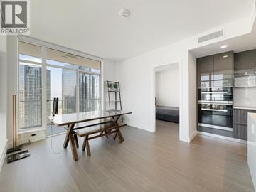 Burnaby apartment for rent - A modern living room with a dining table and a large window overlooking the city.