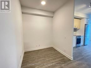 Vaughan (Brownridge) condo for rent - A room with wooden flooring and white walls, with a kitchen visible in the background.
