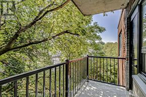 Toronto (The Beaches) condo for rent - A balcony with a black railing and a view of trees and a building.