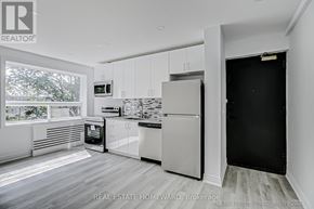 Toronto (The Beaches) condo for rent - A white kitchen with a black door and a window.