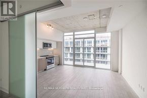 Toronto (South Riverdale) condo for rent - A spacious living room with a kitchen area and sliding glass doors leading to a balcony.