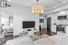 Toronto (Niagara) condo for rent - A modern living room with a flat screen TV and a kitchen area in the background.