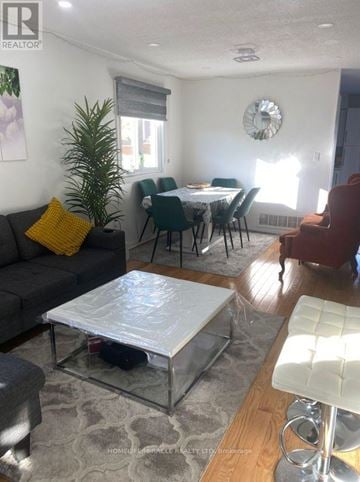 Brampton (Sandringham-Wellington) apartment for rent - A living room with a grey couch, a glass coffee table, and a dining table with chairs.