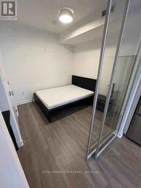Toronto (Waterfront Communities) condo for rent - A bedroom with a bed, wooden flooring, and a glass door.