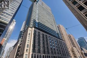 Toronto (Bay Street Corridor) condo for rent - A tall building with a glass facade stands in the middle of a cityscape.