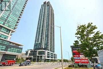 Mississauga (City Centre) condo for rent - A tall building with a glass facade stands in front of a smaller building with a red truck parked in front.