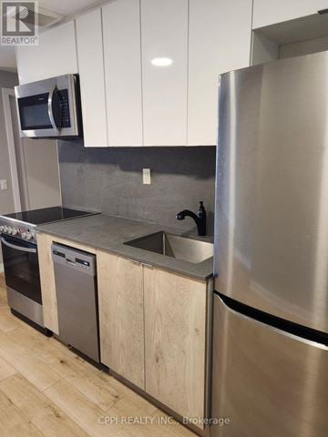 Oshawa (O'neill) condo for rent - A modern kitchen with a stainless steel refrigerator and wooden cabinets.
