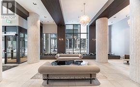 Toronto (Mimico) condo for rent - A modern lobby with a large sofa and pillows, a chandelier, and a glass wall.
