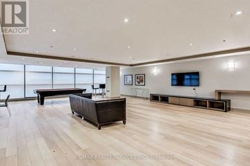 Mississauga (City Centre) condo for rent - A spacious living room with a dark brown sofa and a television mounted on the wall.