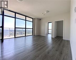 Kitchener condo for rent - A spacious room with wooden flooring and large windows overlooking the city.