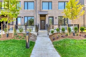 Mississauga (Erin Mills) townhouse for rent - A modern brick building with a black door and windows, surrounded by a well-manicured lawn and trees.