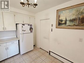 Toronto (Yorkdale-Glen Park) triplex for rent - A kitchen with white cabinets and a fridge with a painting on the wall.