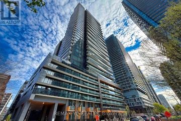 Toronto (Mount Pleasant West) condo for rent - A tall building with a glass facade stands in front of a cloudy sky.