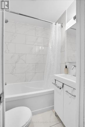 Toronto (South Parkdale) apartment for rent - A white bathroom with a marble tile wall and a glass shower door.