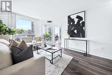 Toronto (Banbury-Don Mills) condo for rent - A living room with a beige couch, a glass coffee table, and a large abstract painting on the wall.