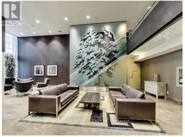 Toronto (Niagara) condo for rent - A modern living room with a large sectional sofa and a coffee table in front of a large abstract painting.
