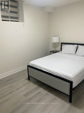 Bradford West Gwillimbury (Bond Head) apartment for rent - A bed with a white comforter and two pillows sits in a room with a lamp and a window.