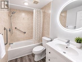 St. Catharines (Lakeport) apartment for rent - A bathroom with a white toilet, a bathtub with a shower head, a sink, and a round mirror.