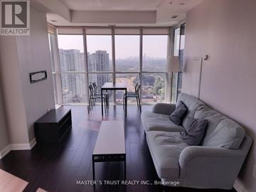 Toronto (Lansing-Westgate) condo for rent - A living room with a grey couch and a table with chairs in front of a large window.