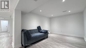 Toronto (Bathurst Manor) apartment for rent - A living room with a grey couch and a brokerage logo on the wall.