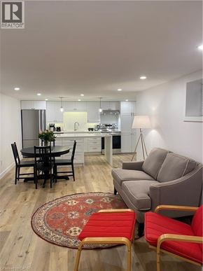 Brantford apartment for rent - A living room with a grey couch, a black dining table and chairs, and a rug with a red chair.