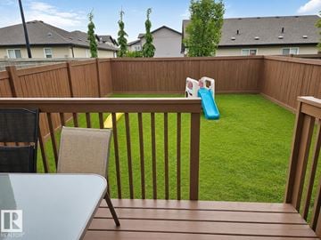 Edmonton duplex for rent - A backyard with a wooden deck, a table, two chairs, a slide, and a green lawn.