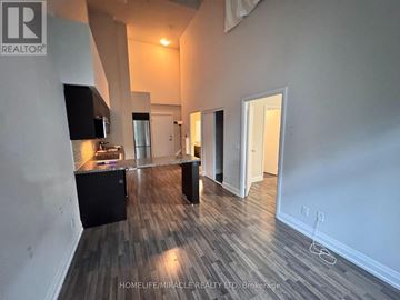Toronto (Clanton Park) condo for rent - A spacious room with wooden flooring and a kitchen area with a counter and cabinets.