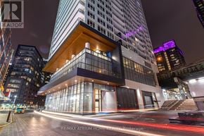 Toronto (Waterfront Communities) condo for rent - A modern building with a glass facade and a wooden balcony is illuminated at night.