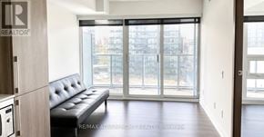Toronto (Waterfront Communities) condo for rent - A black leather sofa sits in a bright room with a window overlooking a cityscape.
