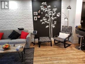 Vaughan (Maple) condo for rent - A living room with a grey couch, a coffee table, and a wall with a tree mural.