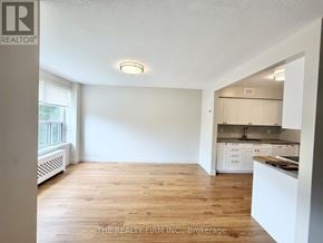 London South (South F) condo for rent - A well-lit, spacious room with wooden flooring and a kitchen area in the background.