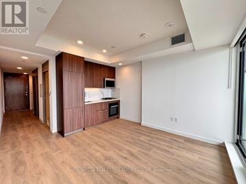 Toronto (Bayview Village) condo for rent - A spacious room with wooden flooring and a kitchen area with a microwave and oven.