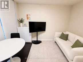 Toronto (Waterfront Communities) condo for rent - A living room with a white couch, a black TV stand, and a white table.