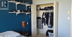 Vancouver apartment for rent - A bedroom with a bed, a lamp, a closet with clothes and a shelf with hats.