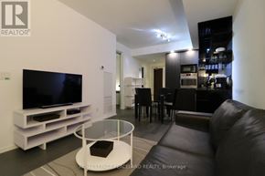 Toronto (Bay Street Corridor) condo for rent - A modern living room with a black leather couch and a television on a white stand.