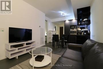 Toronto (Bay Street Corridor) condo for rent - A modern living room with a black leather couch and a television on a white stand.