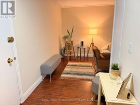 Hamilton (Corman) condo for rent - A room with a white door, a grey bench, a wooden floor, a small table with a plant on it, and a lamp on a side table.