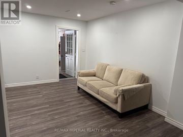 Whitchurch-Stouffville apartment for rent - A beige couch sits in a room with white walls and wood flooring.