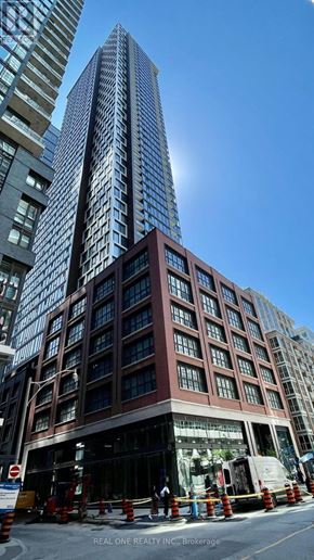Toronto (Waterfront Communities) condo for rent - A tall building with a glass facade stands in front of a shorter building with a brick facade.