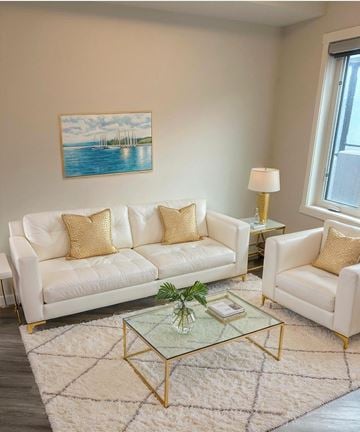 Calgary apartment for rent - A living room with a white sofa, a glass coffee table, and a painting on the wall.