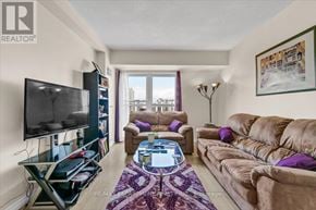 Hamilton (Corktown) condo for rent - A living room with a flat screen TV, a glass coffee table, and a purple rug.