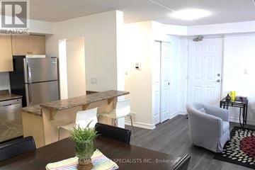 Kitchener condo for rent - A kitchen with a refrigerator, a dining table with chairs, and a living room with a couch.