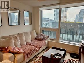 Toronto condo for rent - A living room with a couch, a coffee table, and a window overlooking a cityscape.