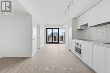 Toronto (Thorncliffe Park) condo for rent - A spacious kitchen with white cabinets and a view of the city through the glass doors.