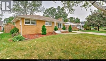Windsor apartment for rent - A house with a brown brick exterior and a white window is surrounded by a green lawn.
